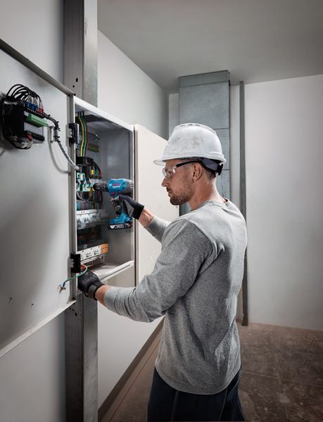 บุคคลที่สวมอุปกรณ์ด้านความปลอดภัยใช้สว่านไร้สายบนแผงควบคุมไฟฟ้า.