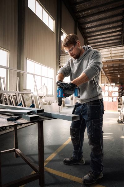 บุคคลที่สวมอุปกรณ์ความปลอดภัยกำลังเจาะคานโลหะในโรงงาน.