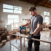 บุคคลที่สวมอุปกรณ์ความปลอดภัยกำลังเจาะเข้าไปในโครงไม้ในโรงงาน.