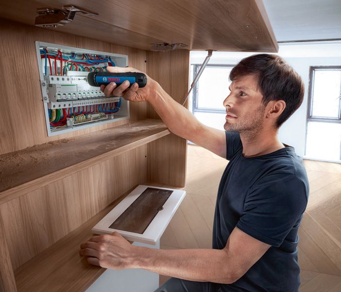 คนใช้ไขควงไร้สายในการยึดส่วนประกอบในแผงไฟฟ้า.