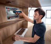 คนใช้ไขควงไร้สายในการยึดส่วนประกอบในแผงไฟฟ้า.