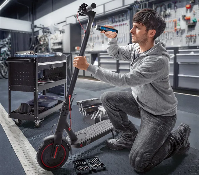 คนกำลังซ่อมสกู๊ตเตอร์ไฟฟ้าโดยใช้ไขควงไร้สายในโรงงาน.