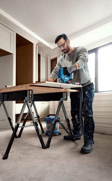 บุคคลที่สวมอุปกรณ์ความปลอดภัยใช้เลื่อยจิ๊กซอว์ตัดไม้บนโต๊ะทำงาน.