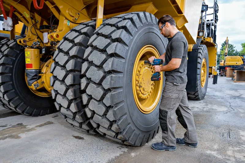บุคคลที่สวมอุปกรณ์ด้านความปลอดภัยใช้ประแจกระแทกกับยางรถยนต์ก่อสร้างขนาดใหญ่.