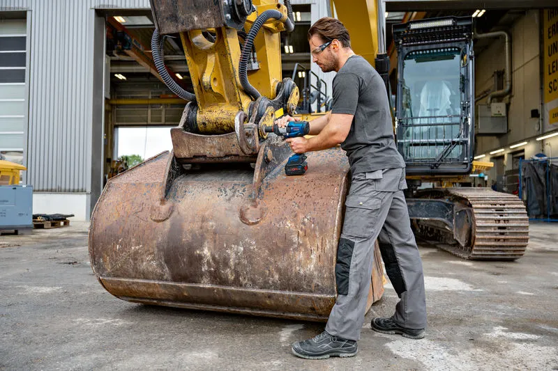 บุคคลที่สวมอุปกรณ์ด้านความปลอดภัยใช้ประแจกระแทกกับเครื่องจักรกลก่อสร้างขนาดหนัก.