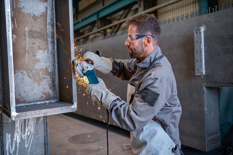 บุคคลที่สวมอุปกรณ์ด้านความปลอดภัยกำลังเจียรโลหะด้วยเครื่องเจียรแบบมุม ทำให้เกิดประกายไฟ.