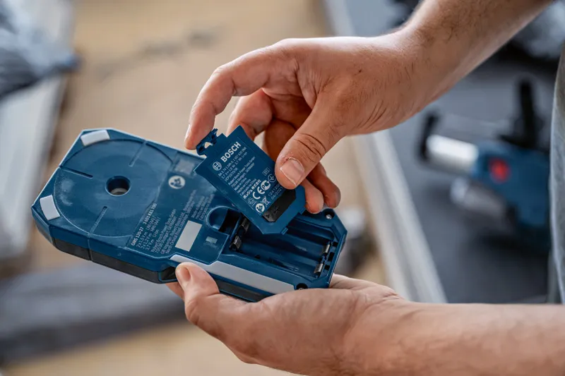 บุคคลดังกล่าวใส่ชุดแบตเตอรี่เข้าไปในตัวเรือนเครื่องมือไฟฟ้าสีน้ำเงิน.