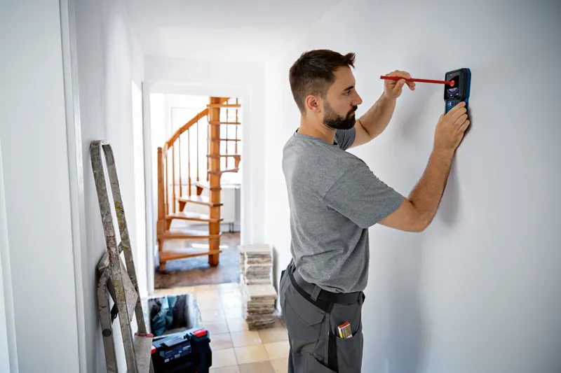 คนกำลังทำเครื่องหมายบนผนังด้วยดินสอขณะใช้เครื่องมือตรวจจับ.