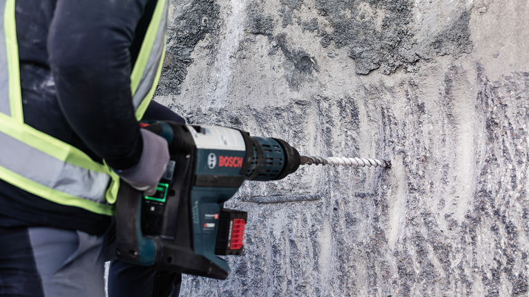 บุคคลที่สวมอุปกรณ์ความปลอดภัยกำลังเจาะเข้าไปในผนังคอนกรีตโดยใช้เครื่องมือไฟฟ้า