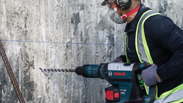 ผู้ที่สวมอุปกรณ์ความปลอดภัยกำลังเจาะเข้าไปในผนังคอนกรีต