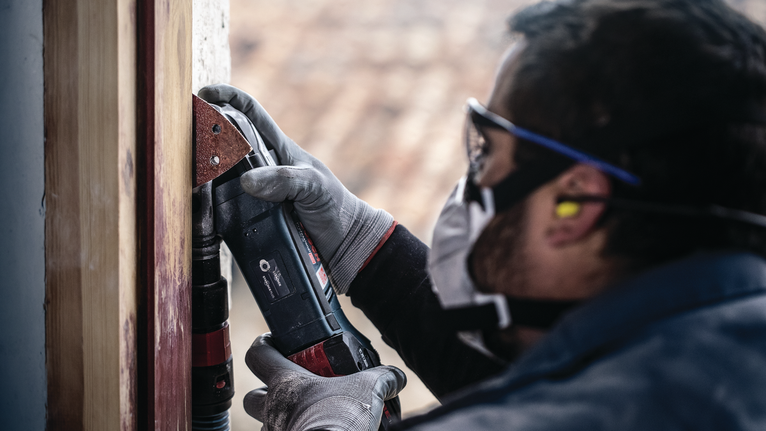 บุคคลที่สวมอุปกรณ์ความปลอดภัยกำลังขัดกรอบไม้โดยใช้เครื่องมือไฟฟ้า