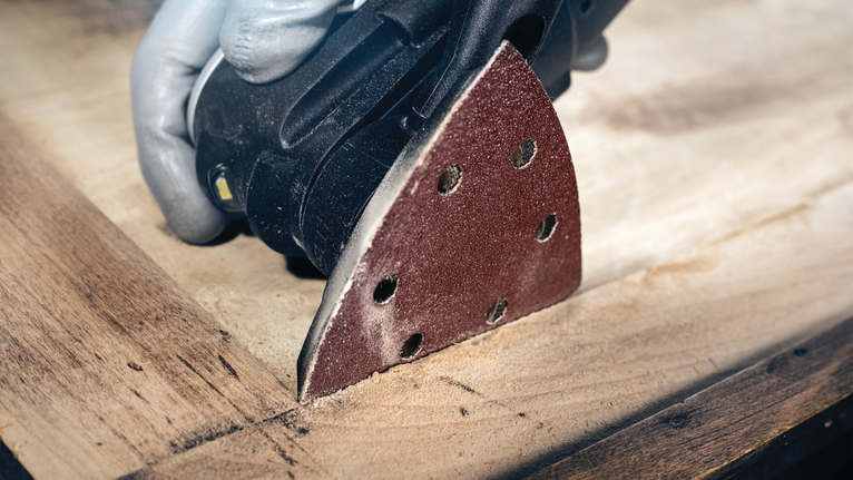 บุคคลที่สวมอุปกรณ์ป้องกันความปลอดภัยขัดพื้นผิวไม้ด้วยเครื่องขัดรายละเอียด