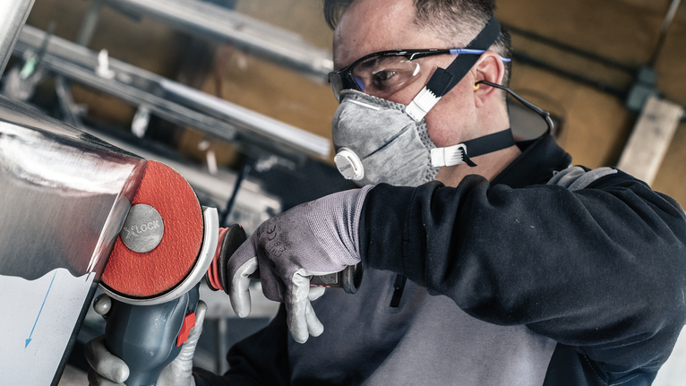 บุคคลที่สวมอุปกรณ์ความปลอดภัยกำลังขัดโลหะด้วยเครื่องมือไฟฟ้า