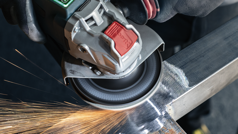 บุคคลที่สวมอุปกรณ์ความปลอดภัยทำการบดโลหะ ทำให้เกิดประกายไฟ