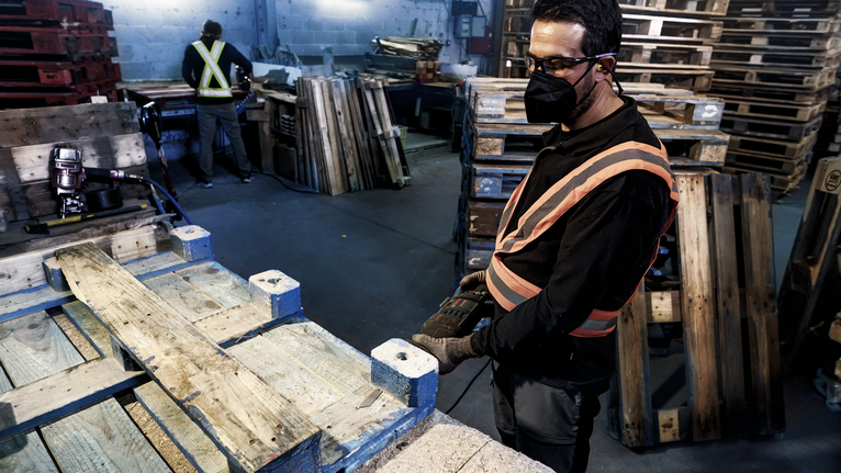 บุคคลที่สวมอุปกรณ์ด้านความปลอดภัยใช้เครื่องมือไฟฟ้าในการทำงานบนพาเลทไม้