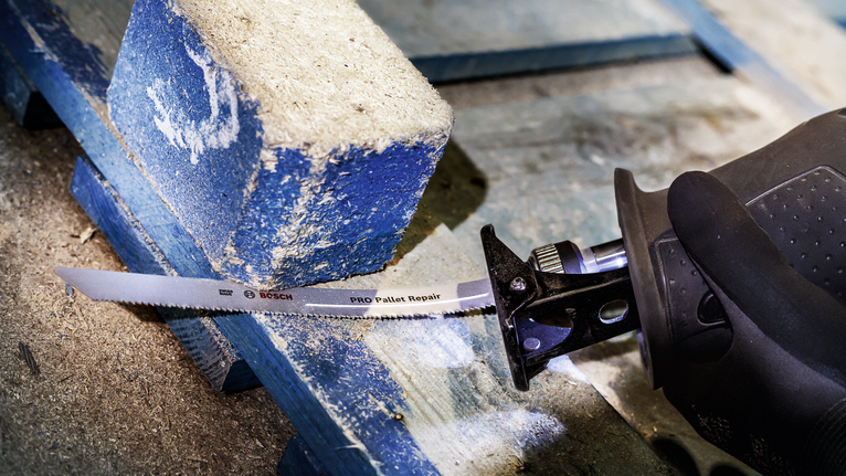 บุคคลที่สวมอุปกรณ์ความปลอดภัยกำลังตัดพาเลทไม้ด้วยเลื่อยตัดโลหะ