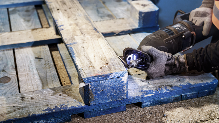 บุคคลที่สวมอุปกรณ์ความปลอดภัยกำลังตัดพาเลทไม้ด้วยเลื่อยตัดโลหะ