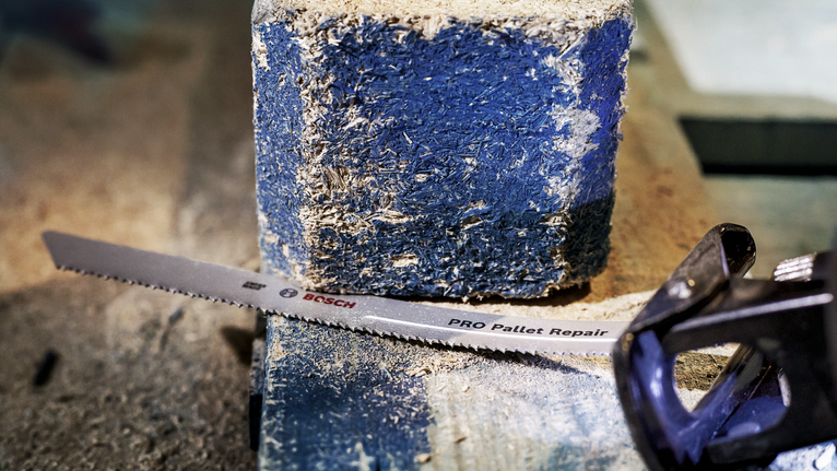 ใบเลื่อยตัดโลหะวางอยู่บนแท่นพาเลทไม้ที่เต็มไปด้วยฝุ่น