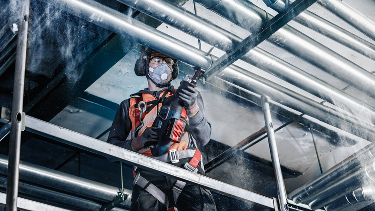 บุคคลที่สวมอุปกรณ์ความปลอดภัยกำลังเจาะท่อเพดานในไซต์ก่อสร้าง