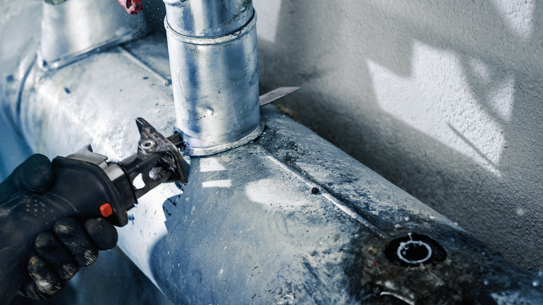 บุคคลที่สวมอุปกรณ์ความปลอดภัยตัดท่อโลหะด้วยเครื่องมือไฟฟ้า