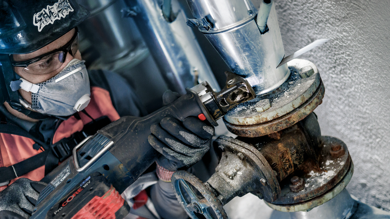 บุคคลที่สวมอุปกรณ์ด้านความปลอดภัยใช้เลื่อยตัดท่อที่เป็นสนิม