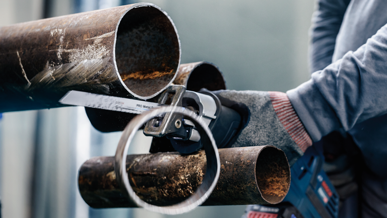 บุคคลที่สวมอุปกรณ์ความปลอดภัยใช้เลื่อยไฟฟ้าตัดท่อเหล็ก