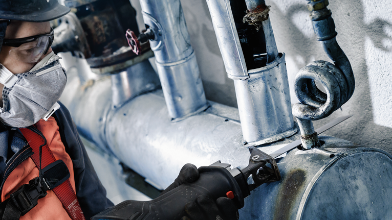 บุคคลที่สวมอุปกรณ์ความปลอดภัยตัดท่อโลหะด้วยเครื่องมือไฟฟ้า