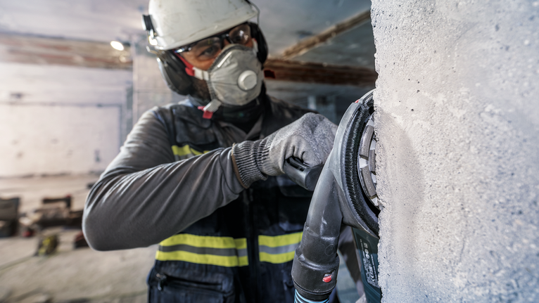 บุคคลที่สวมอุปกรณ์ความปลอดภัยกำลังเจียรผนังคอนกรีตด้วยเครื่องมือไฟฟ้า