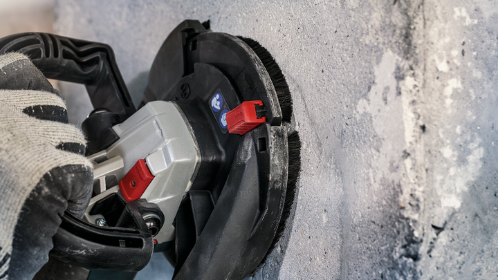 บุคคลที่สวมอุปกรณ์ด้านความปลอดภัยใช้เครื่องมือไฟฟ้าขัดผนังคอนกรีต