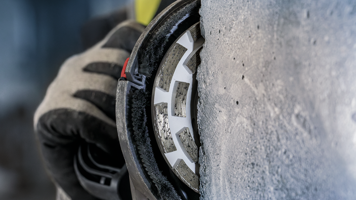 บุคคลที่สวมอุปกรณ์ความปลอดภัยกำลังเจียรคอนกรีตด้วยล้อเพชร