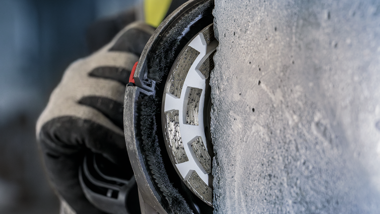 บุคคลที่สวมอุปกรณ์ความปลอดภัยกำลังเจียรคอนกรีตด้วยล้อเพชร