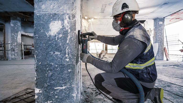 บุคคลที่สวมอุปกรณ์ความปลอดภัยกำลังบดเสาคอนกรีตที่ไซต์ก่อสร้าง