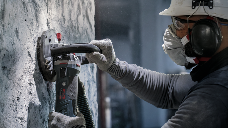 บุคคลที่สวมอุปกรณ์ความปลอดภัยกำลังเจียรผนังคอนกรีตด้วยเครื่องมือไฟฟ้า