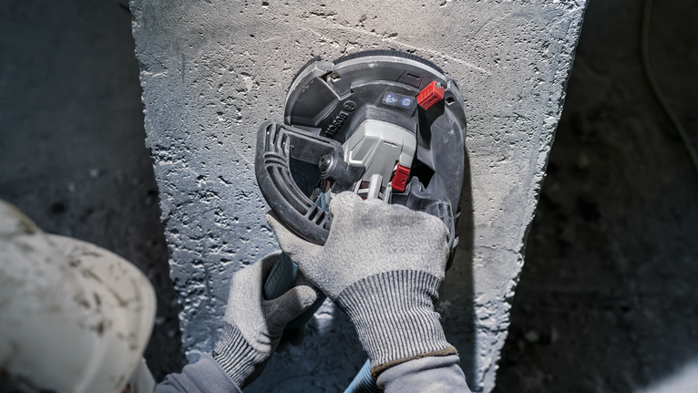 บุคคลที่สวมอุปกรณ์ความปลอดภัยกำลังบดคอนกรีตด้วยเครื่องมือไฟฟ้า