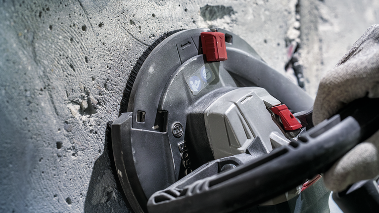 บุคคลที่สวมอุปกรณ์ความปลอดภัยกำลังเจียรผนังคอนกรีตด้วยเครื่องมือไฟฟ้า