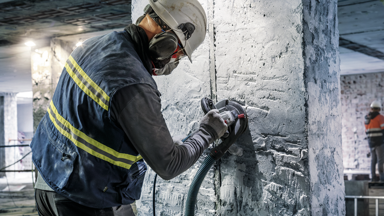 บุคคลที่สวมอุปกรณ์ความปลอดภัยกำลังบดเสาคอนกรีตด้วยเครื่องมือไฟฟ้า