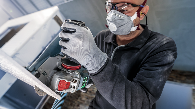 บุคคลที่สวมอุปกรณ์ด้านความปลอดภัยกำลังขัดพื้นผิวโดยใช้เครื่องมือไฟฟ้า