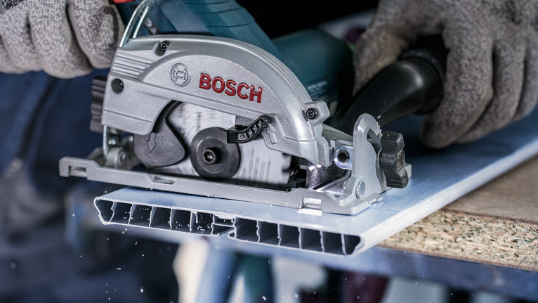 บุคคลที่สวมอุปกรณ์ความปลอดภัยกำลังตัดแผ่นโลหะด้วยเลื่อยวงเดือน