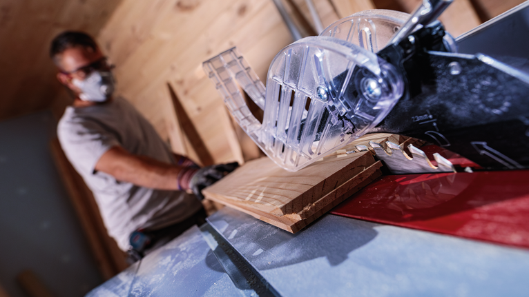 บุคคลที่สวมอุปกรณ์ความปลอดภัยกำลังตัดไม้ด้วยเลื่อยโต๊ะ