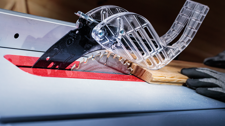 โต๊ะเลื่อยตัดไม้ คนสวมอุปกรณ์นิรภัยคอยนำทางวัสดุ