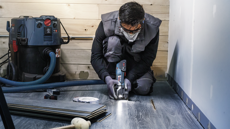 บุคคลที่สวมอุปกรณ์ความปลอดภัยกำลังตัดพื้นไม้ลามิเนตด้วยเครื่องมือไฟฟ้า