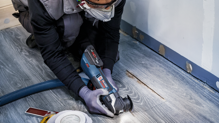 บุคคลที่สวมอุปกรณ์ความปลอดภัยกำลังตัดพื้นไม้ด้วยเครื่องมือไฟฟ้า