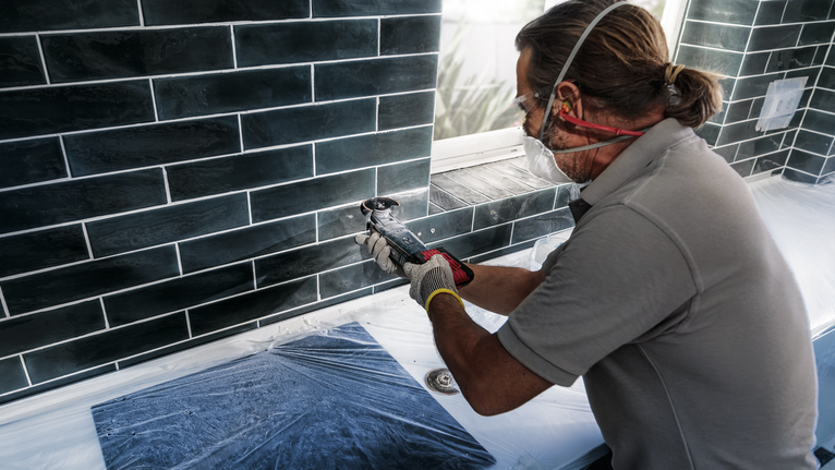 บุคคลที่สวมอุปกรณ์ความปลอดภัยใช้เครื่องมือไฟฟ้าตัดกระเบื้องใต้หน้าต่าง