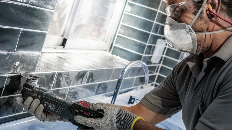 บุคคลที่สวมอุปกรณ์ด้านความปลอดภัยใช้เครื่องมือไฟฟ้าตัดกระเบื้องใกล้อ่างล้างจาน