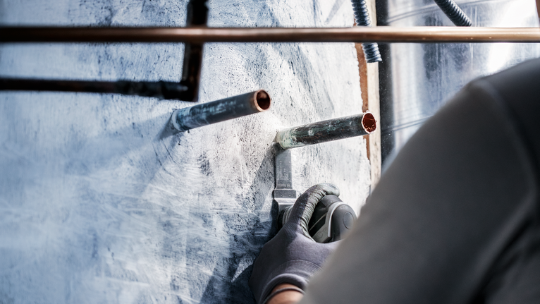 บุคคลที่สวมอุปกรณ์ด้านความปลอดภัยใช้เครื่องมือไฟฟ้าตัดผนังรอบท่อโลหะ