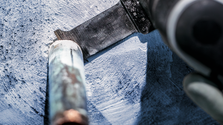 บุคคลที่สวมอุปกรณ์ความปลอดภัยกำลังตัดท่อโลหะด้วยเลื่อยตัดโลหะแบบลูกสูบ