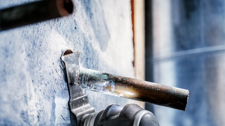 เครื่องมือไฟฟ้าตัดผ่านท่อโลหะที่ยื่นออกมาจากผนังคอนกรีต