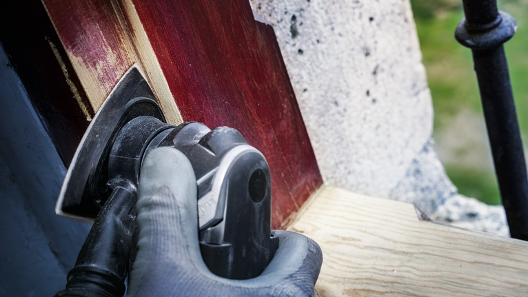 บุคคลที่สวมอุปกรณ์ความปลอดภัยกำลังขัดไม้ทาสีด้วยเครื่องมือไฟฟ้า