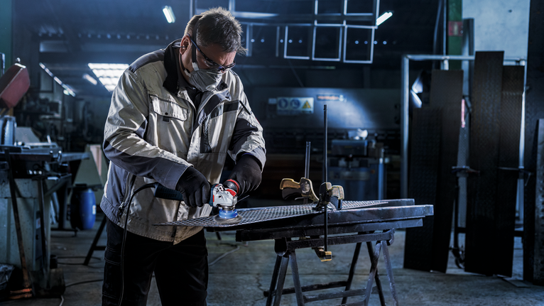 บุคคลที่สวมอุปกรณ์ความปลอดภัยกำลังเจียรแผ่นโลหะในโรงงาน