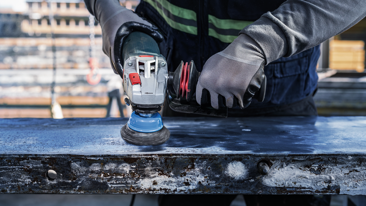 บุคคลที่สวมอุปกรณ์ด้านความปลอดภัยขัดพื้นผิวโลหะด้วยเครื่องมือไฟฟ้า